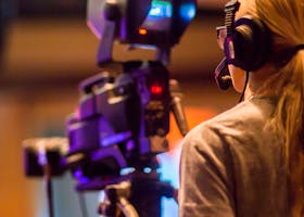 A woman operates a professional camera indoors, focusing on media production.